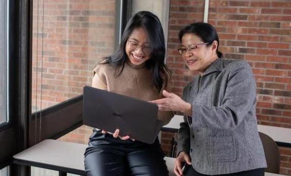 一位新葡新京娱乐场app下载的学生和她的导师一起看着一台笔记本电脑，面带微笑